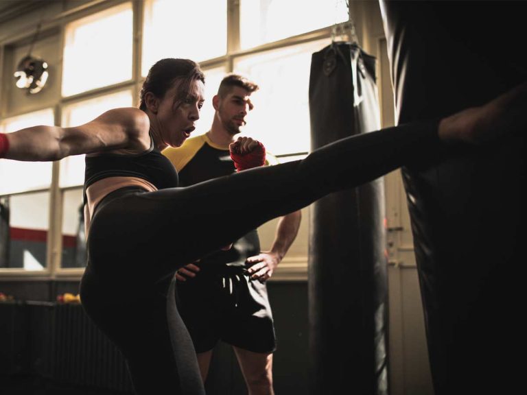 A male trainer watches his female student's kickboxing form.