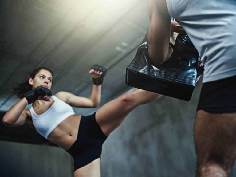 A woman performs a high kick while training kickboxing with an instructor.