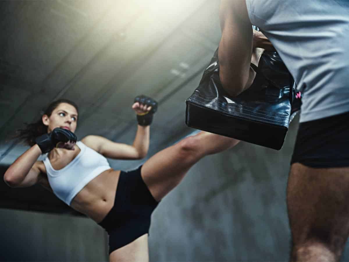 A woman performs a high kick while training kickboxing with an instructor.